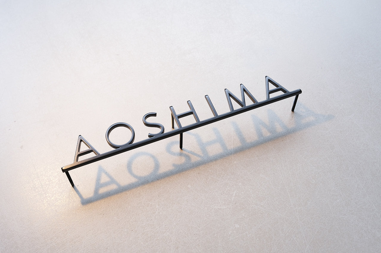 Custom metal sign displaying text in a sleek, modern font. Floating metal letters mounted on a light-colored textured background. Minimalist design suitable for home or business decor.