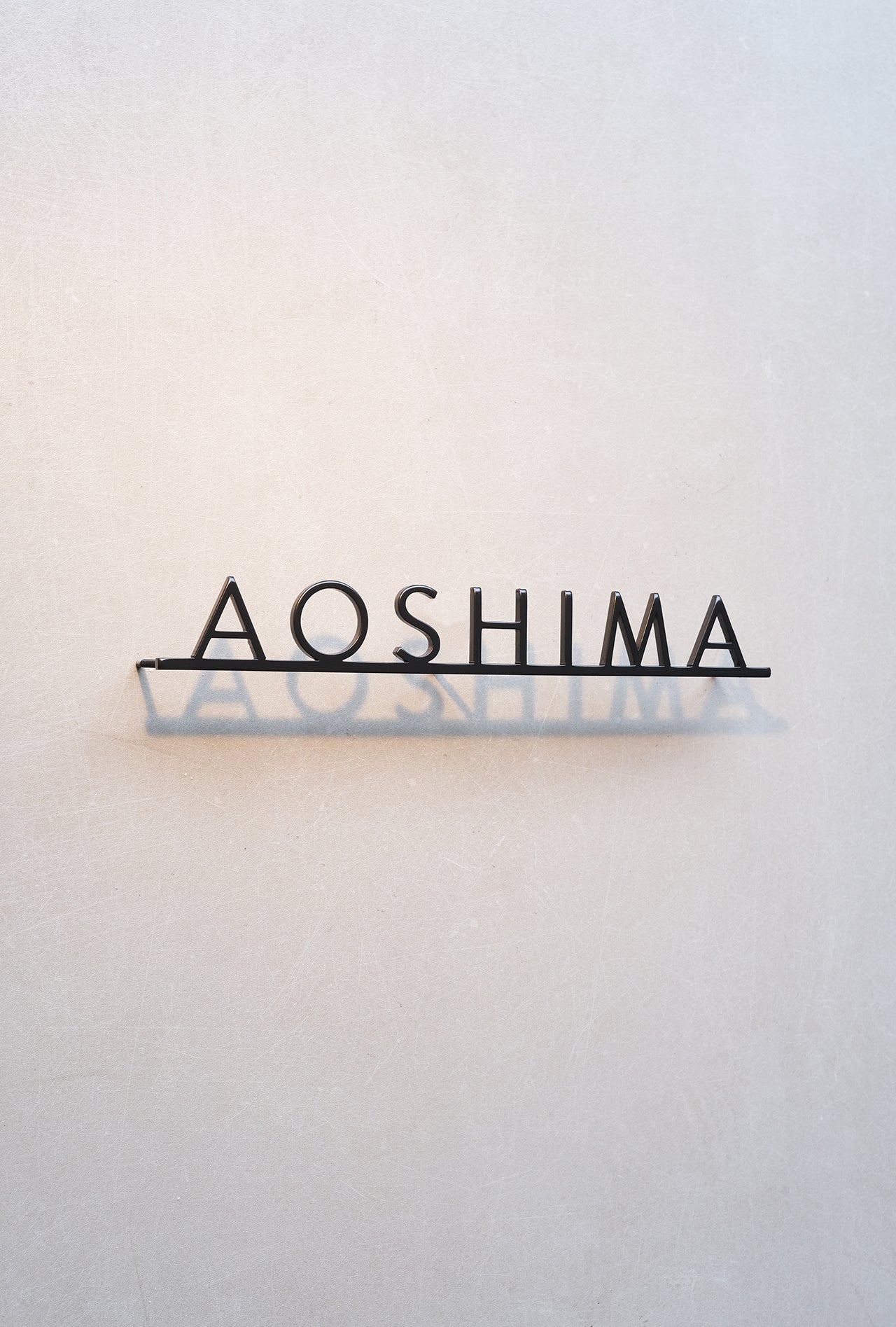 Custom metal sign displaying text in a sleek, modern font. Floating metal letters mounted on a light-colored textured background. Minimalist design suitable for home or business decor.