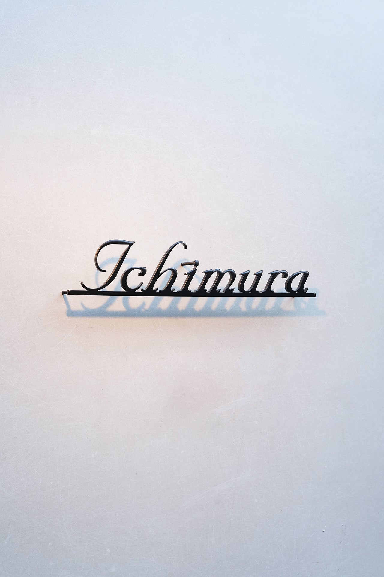 Custom metal sign displaying text in a sleek, modern font. Floating metal letters mounted on a light-colored textured background. Minimalist design suitable for home or business decor.