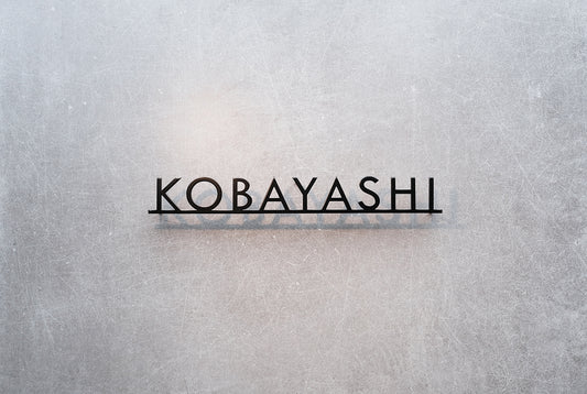 Custom metal sign displaying text in a sleek, modern font. Floating metal letters mounted on a light-colored textured background. Minimalist design suitable for home or business decor.