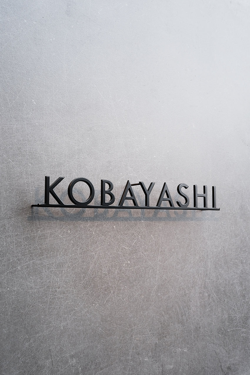 Custom metal sign displaying text in a sleek, modern font. Floating metal letters mounted on a light-colored textured background. Minimalist design suitable for home or business decor.