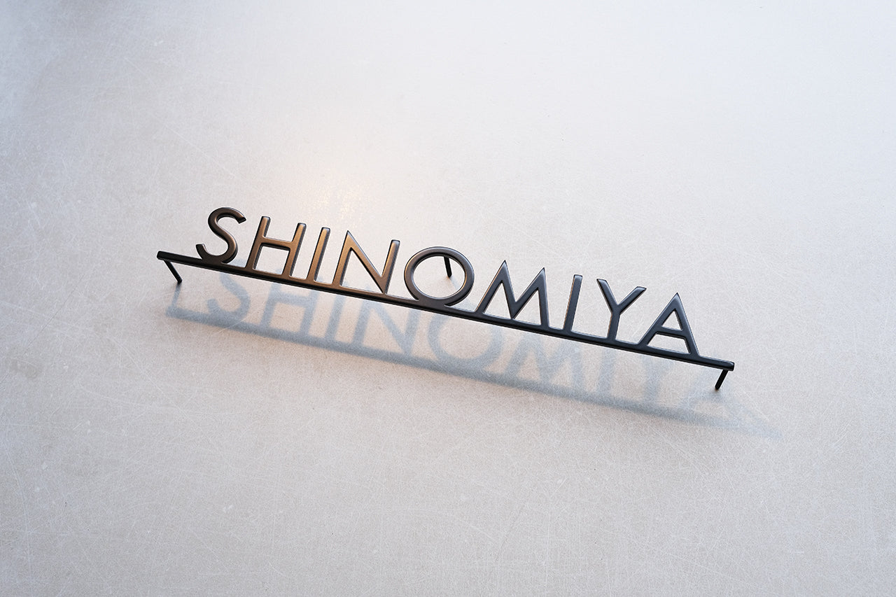Custom metal sign displaying text in a sleek, modern font. Floating metal letters mounted on a light-colored textured background. Minimalist design suitable for home or business decor.