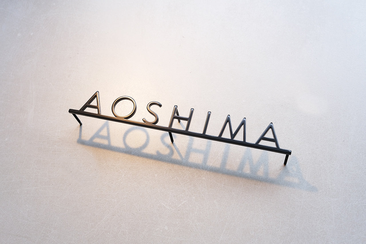Custom metal sign displaying text in a sleek, modern font. Floating metal letters mounted on a light-colored textured background. Minimalist design suitable for home or business decor.