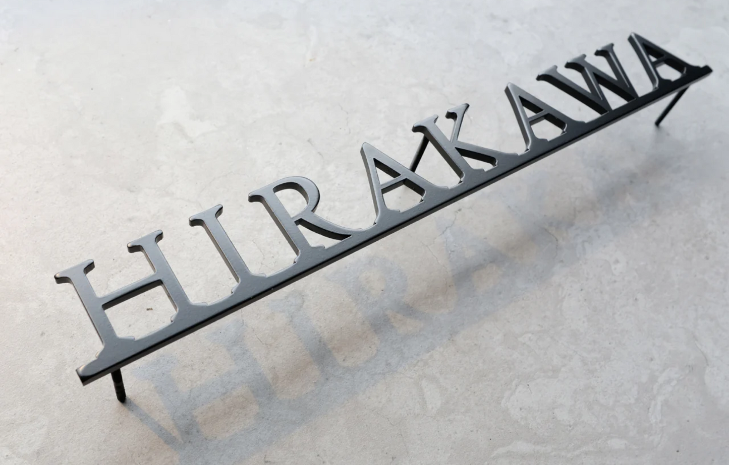 Custom metal sign displaying text in a sleek, modern font. Floating metal letters mounted on a light-colored textured background. Minimalist design suitable for home or business decor.