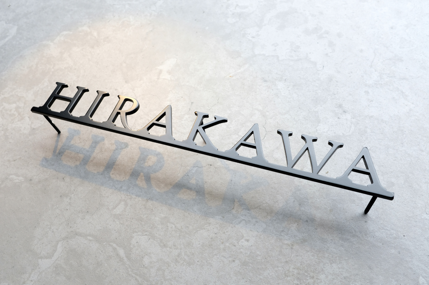 Custom metal sign displaying text in a sleek, modern font. Floating metal letters mounted on a light-colored textured background. Minimalist design suitable for home or business decor.