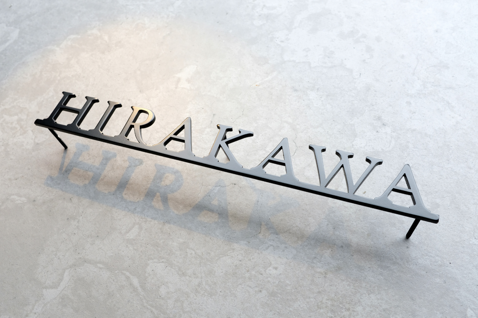 Custom metal sign displaying text in a sleek, modern font. Floating metal letters mounted on a light-colored textured background. Minimalist design suitable for home or business decor.