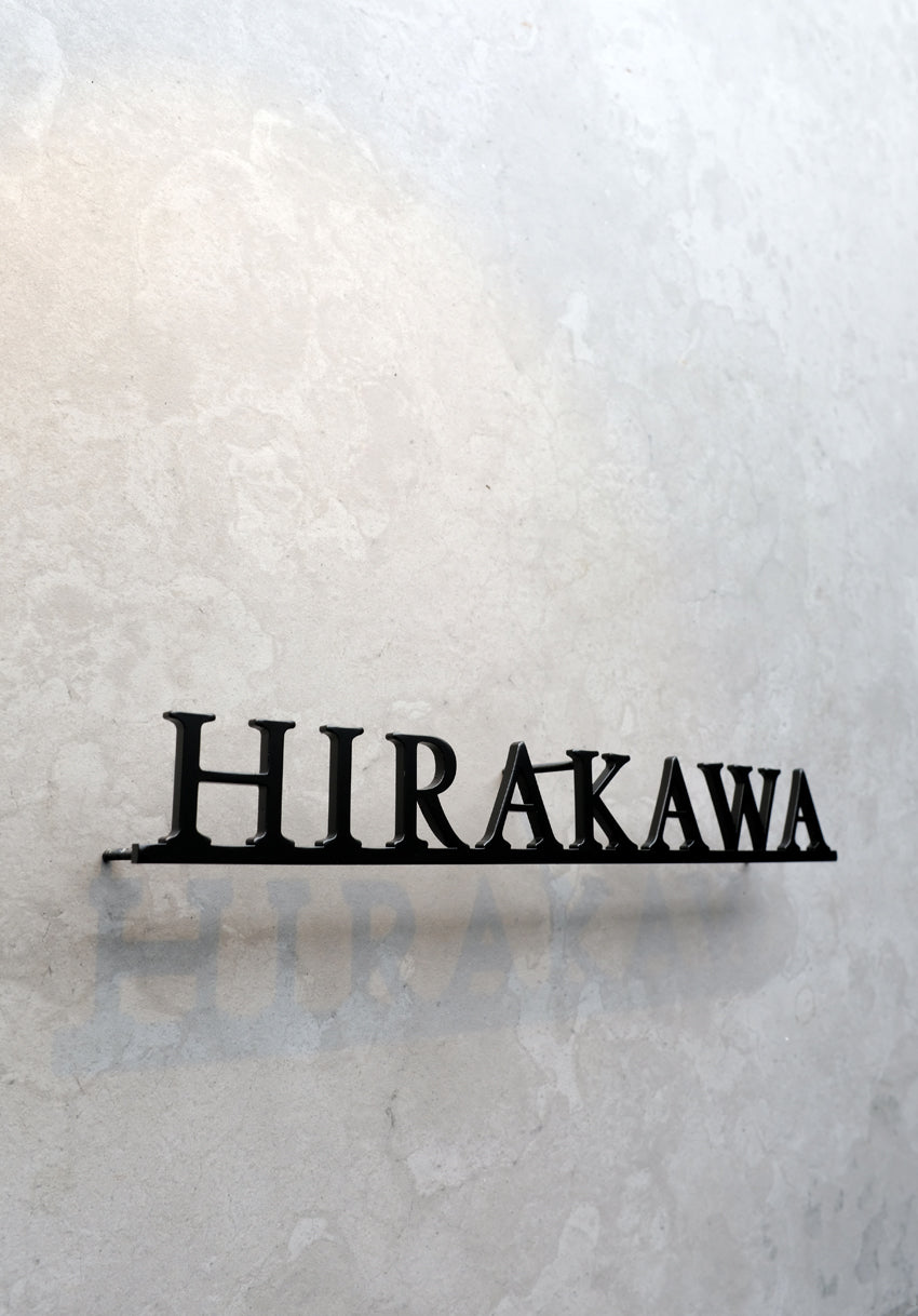 Custom metal sign displaying text in a sleek, modern font. Floating metal letters mounted on a light-colored textured background. Minimalist design suitable for home or business decor.
