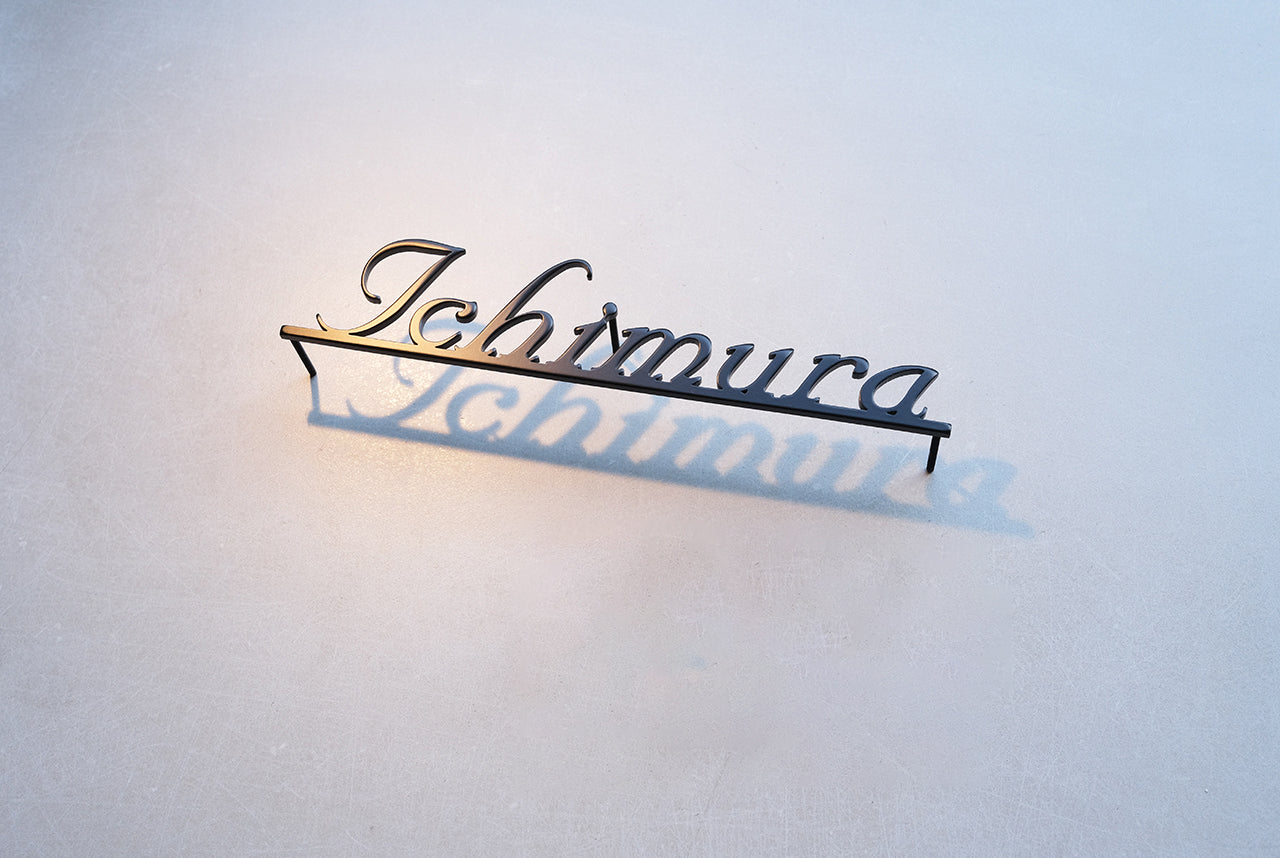 Custom metal sign displaying text in a sleek, modern font. Floating metal letters mounted on a light-colored textured background. Minimalist design suitable for home or business decor.