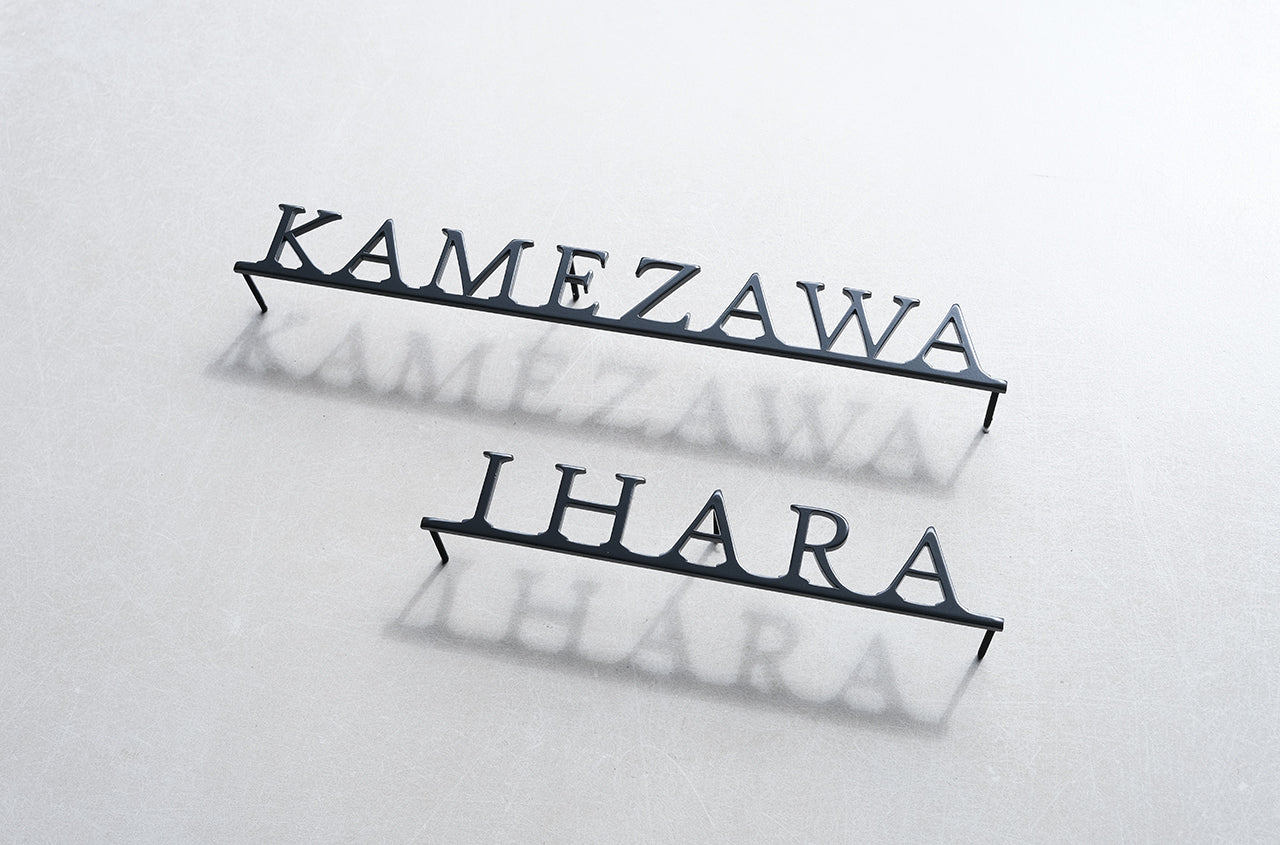 Custom metal sign displaying text in a sleek, modern font. Floating metal letters mounted on a light-colored textured background. Minimalist design suitable for home or business decor.