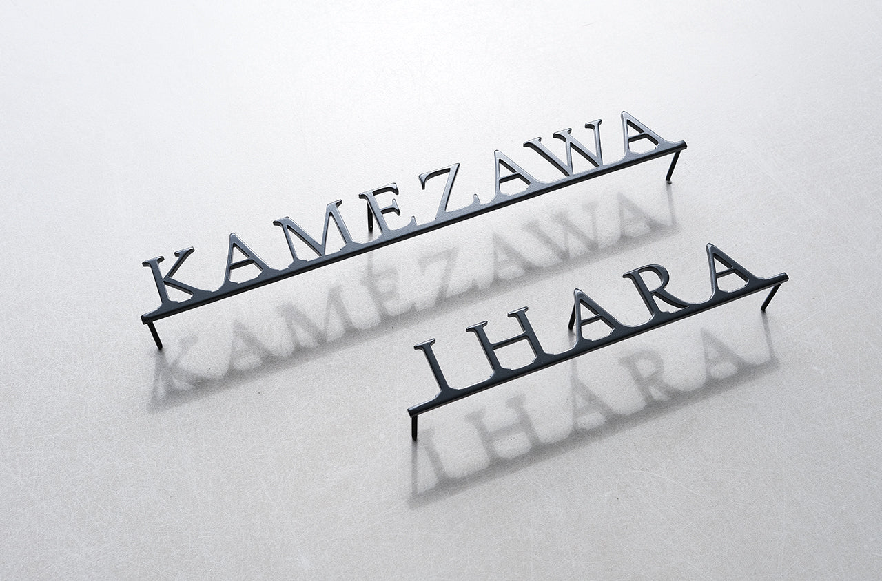 Custom metal sign displaying text in a sleek, modern font. Floating metal letters mounted on a light-colored textured background. Minimalist design suitable for home or business decor.