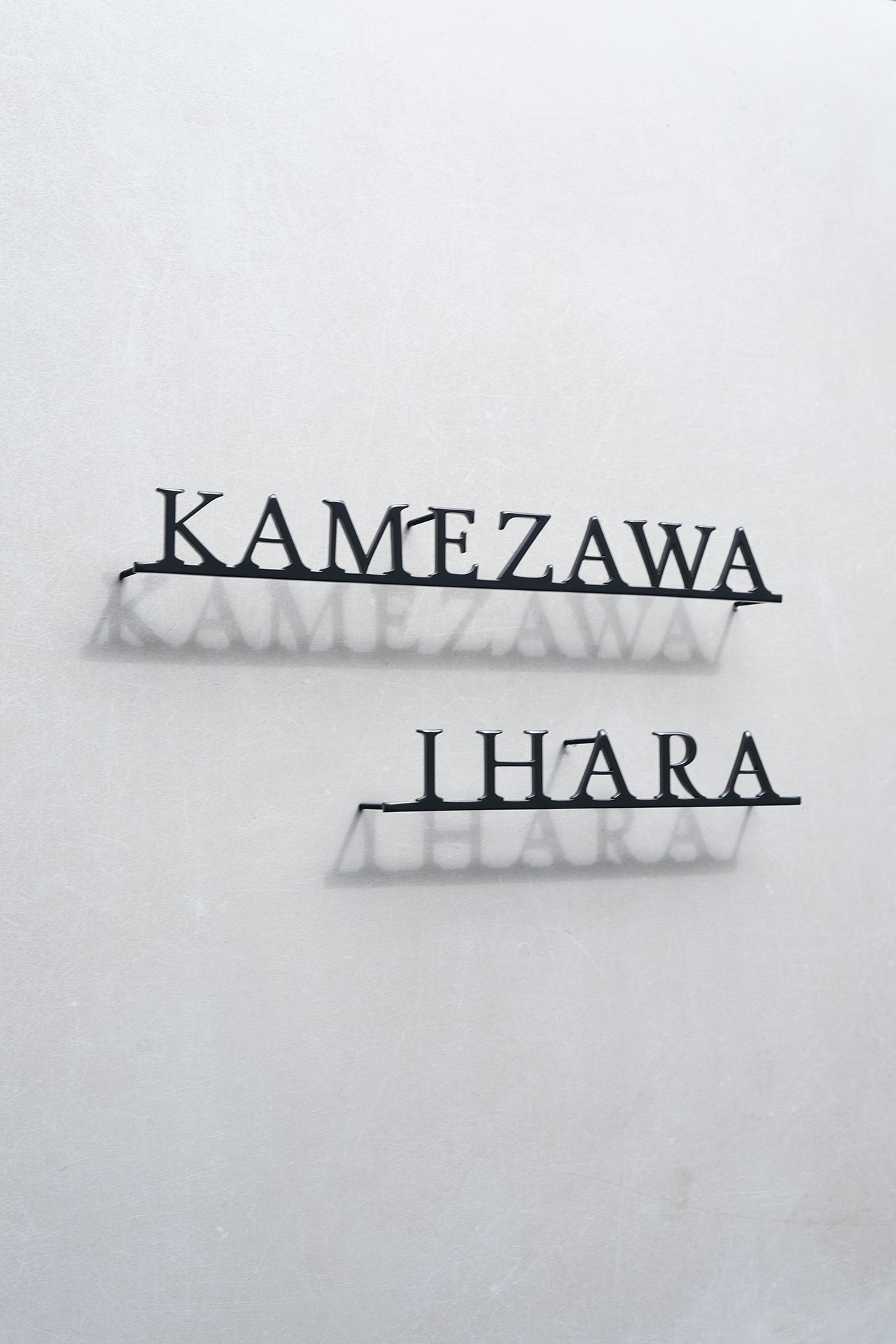 Custom metal sign displaying text in a sleek, modern font. Floating metal letters mounted on a light-colored textured background. Minimalist design suitable for home or business decor.