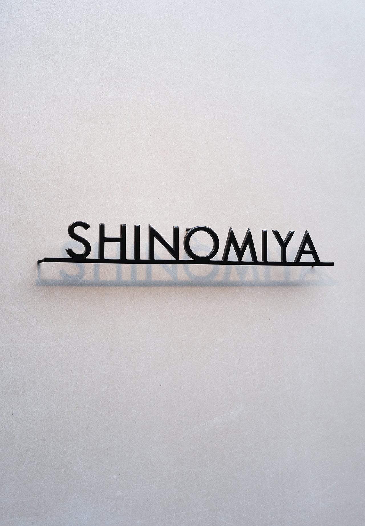 Custom metal sign displaying text in a sleek, modern font. Floating metal letters mounted on a light-colored textured background. Minimalist design suitable for home or business decor.