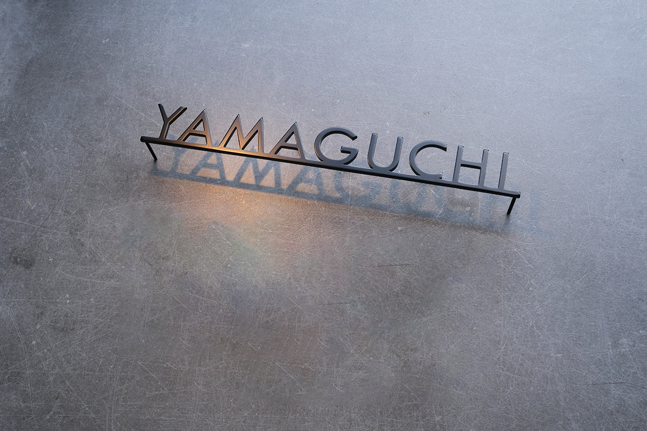 Custom metal sign displaying text in a sleek, modern font. Floating metal letters mounted on a light-colored textured background. Minimalist design suitable for home or business decor.